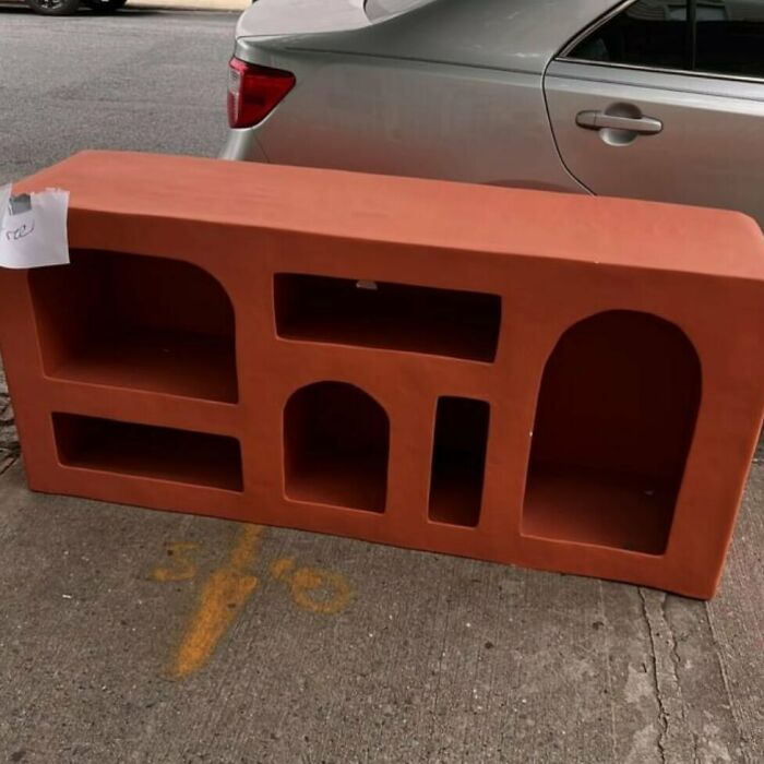 Red shelf with arch-shaped openings left on the curb in NYC, offering a treasure to find for stooping enthusiasts.