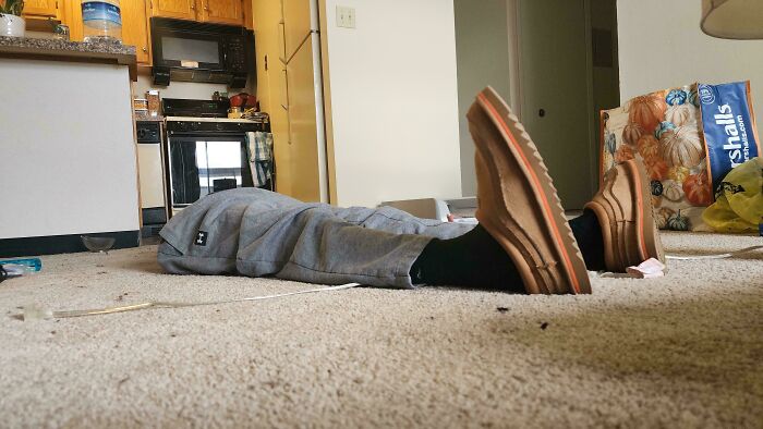 Person lying on the floor in gray pants with shoes, creating an optical illusion that appears confusing at first glance.