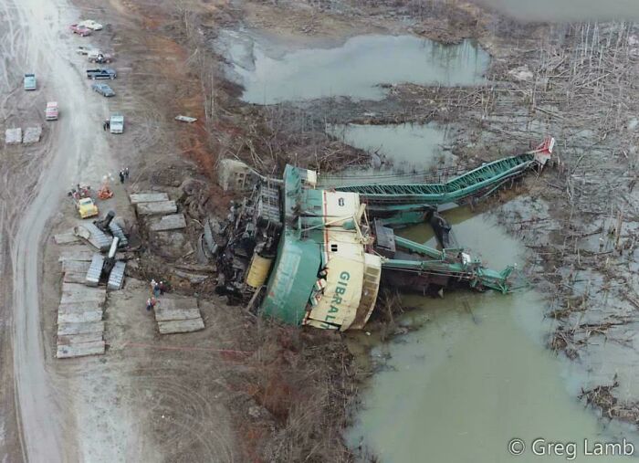 A large industrial machine overturned in muddy waters, surrounded by debris, indicating a costly mishap.