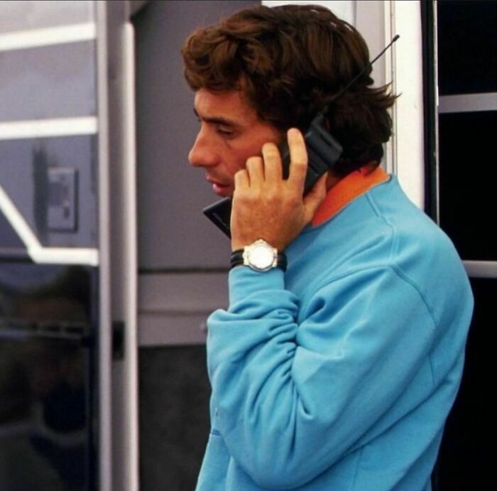 Person in a blue sweater using a vintage '90s mobile phone, embodying a classic moment from the '90s era.