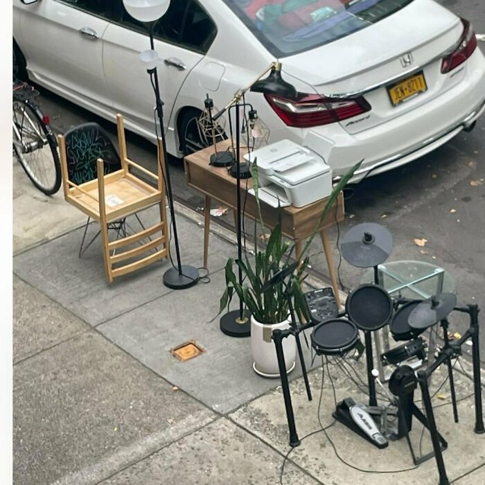 Curbside treasures in NYC include a drum set, lamp, chair, and potted plant waiting for new owners.