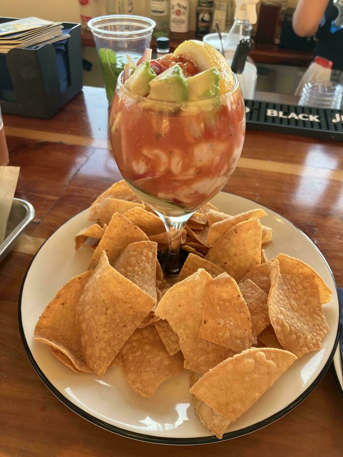 Shrimp cocktail served in a wine glass surrounded by tortilla chips on a white plate in a restaurant setting.