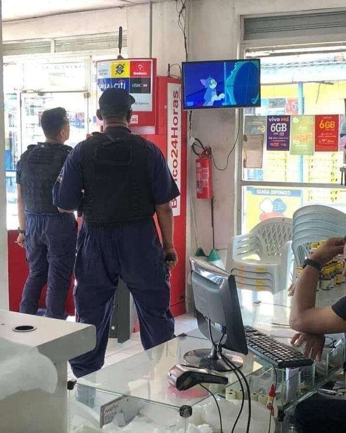 Two officers in blue uniforms watch a cartoon on a TV screen in a store. "Pics That Go Hard" content.