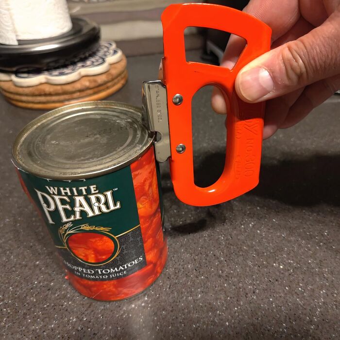 Durable can opener with an orange handle opening a can of White Pearl chopped tomatoes on a kitchen counter.