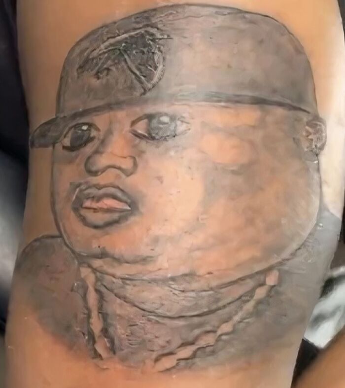Tattoo of a person's face wearing a cap and a chain, shared in a Facebook group discussing undesirable tattoos.
