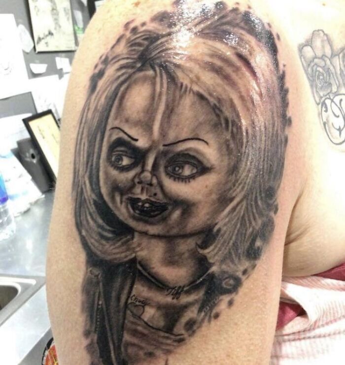 Tattoo of an exaggerated doll-like face on an arm, featured in a Facebook group for unusual tattoos.