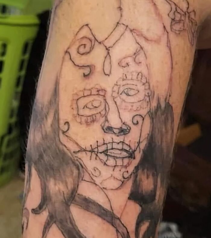Poorly drawn tattoo of a face with lines and swirls on arm, shared in Facebook group for bad tattoos.