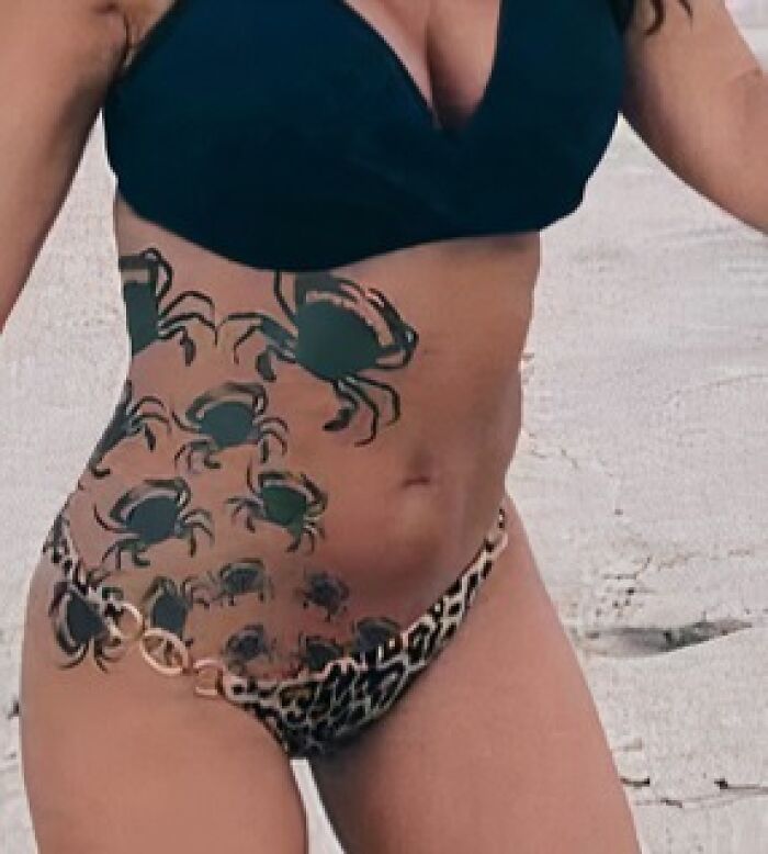 Person with multiple crab tattoos on the torso, wearing a bikini at the beach.