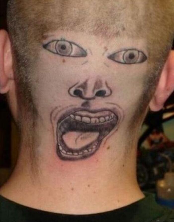Unusual tattoo of a face with open mouth and eyes on the back of a shaved head, shared in a Facebook group.