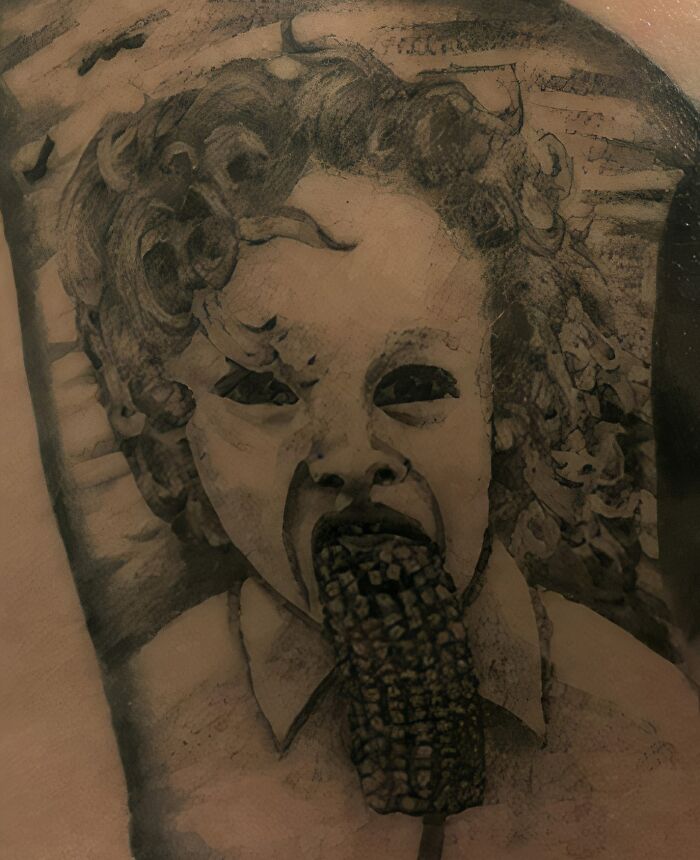 Unusual tattoo of a child with dark eyes eating corn, featured in a Facebook group sharing tattoos they believe shouldn't exist.
