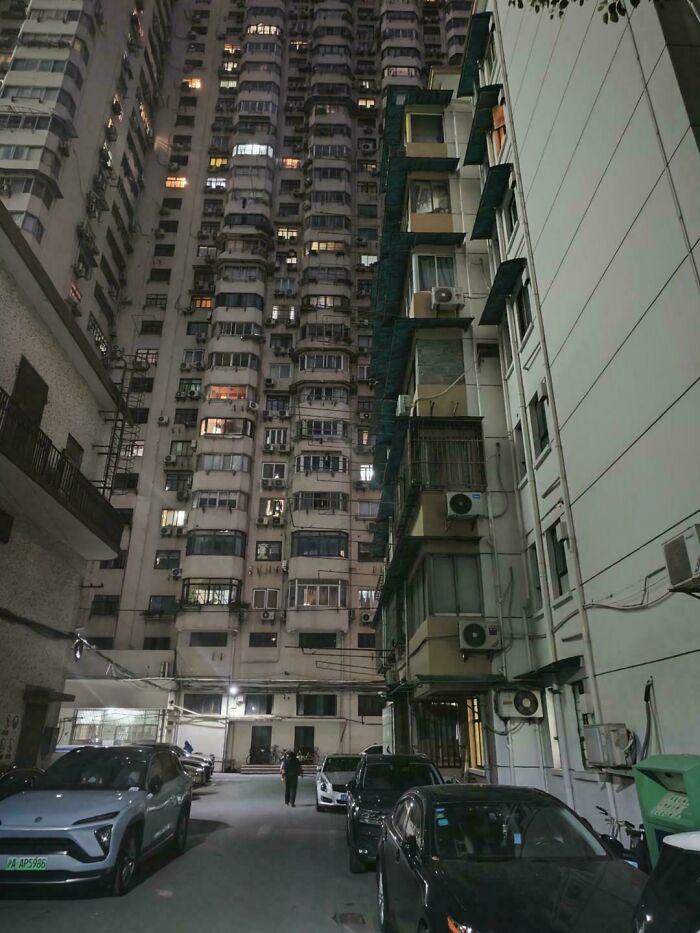 Tall, crowded apartment buildings line a dimly lit urban street, symbolizing an urban hellscape.