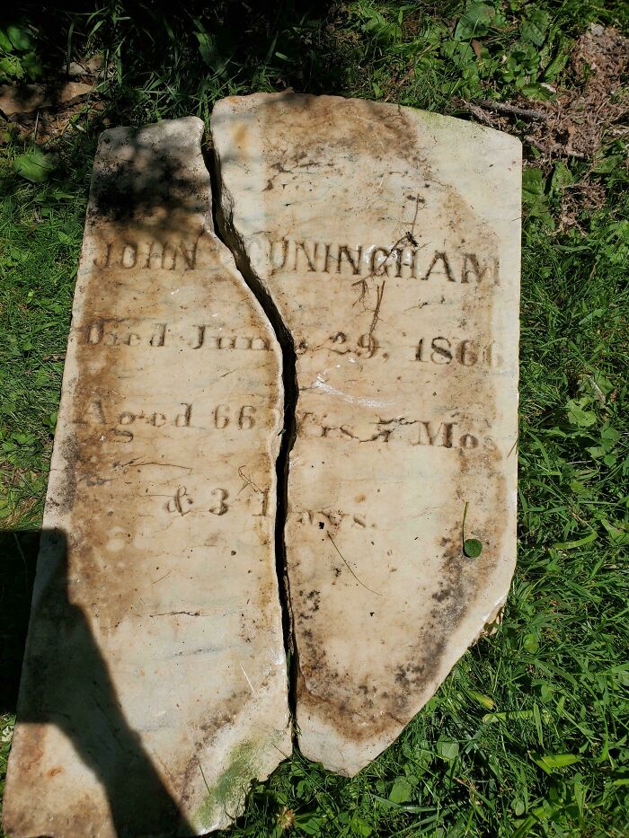 A cracked, weathered tombstone with faded inscription "JOHN CUNINGHAM" and dates. Creepy image from a graveyard.