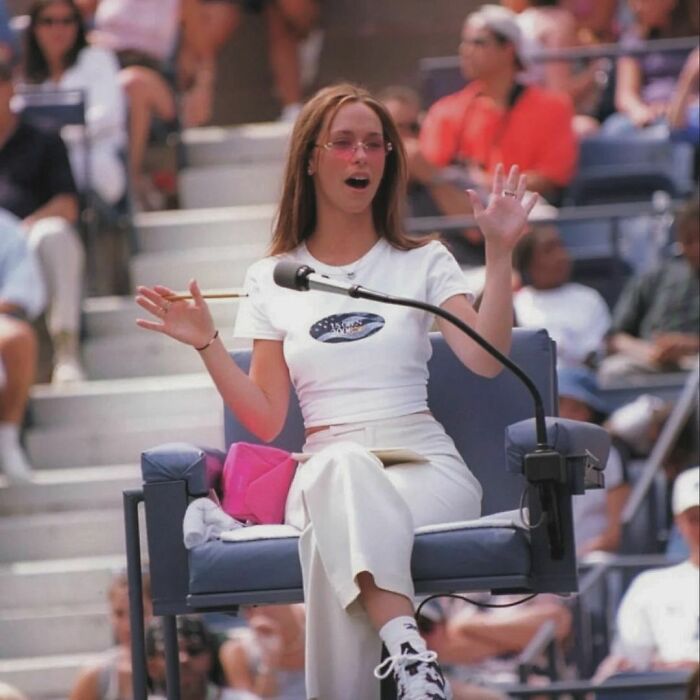 Referee sitting on a chair, gesturing animatedly during a '90s event, surrounded by a crowd.