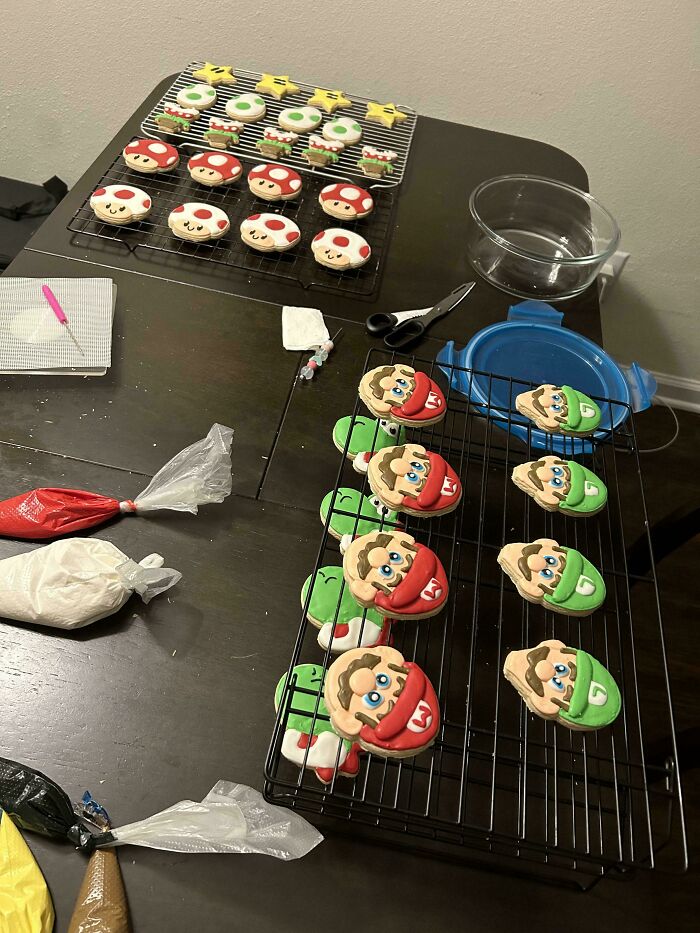 Decorated baking cookies inspired by video game characters on cooling racks with piping bags and tools on a dark table.