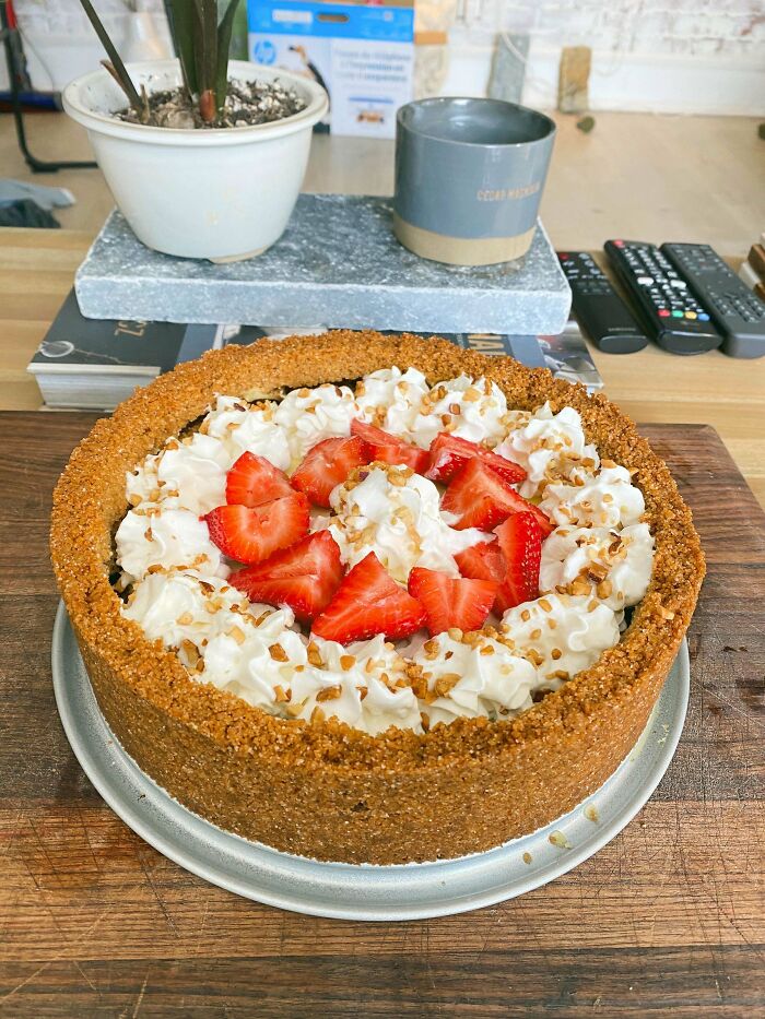 Strawberry dessert with whipped cream and nut topping in a crumb crust, showcasing baking at its finest on a wooden table.