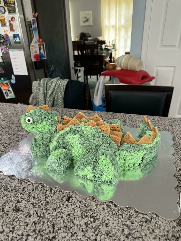 Green dinosaur-shaped cake decorated with star-shaped frosting and graham cracker spikes on a kitchen countertop, baking at its finest.