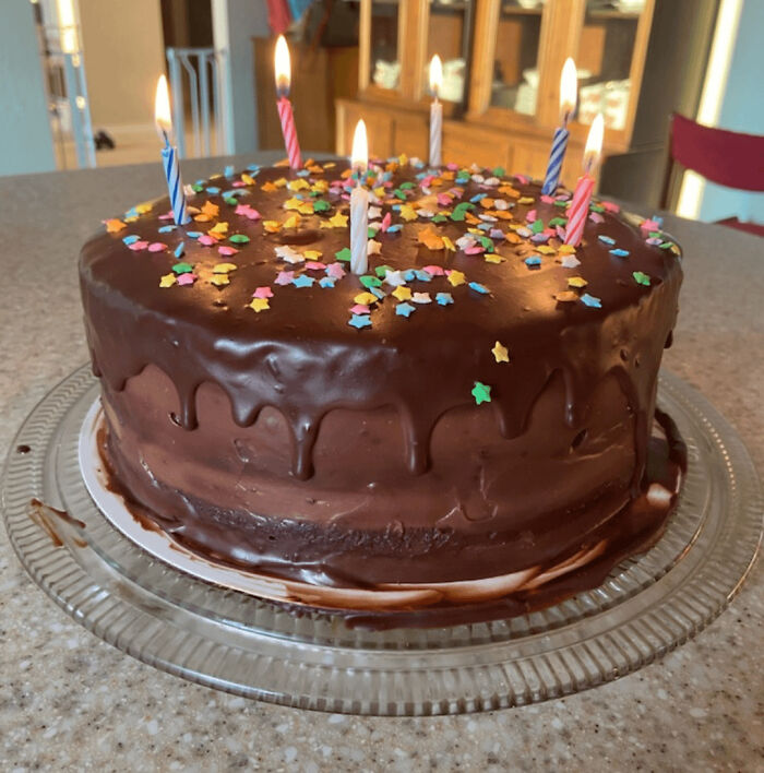 Chocolate birthday cake with star-shaped sprinkles and lit candles, showcasing baking at its finest.