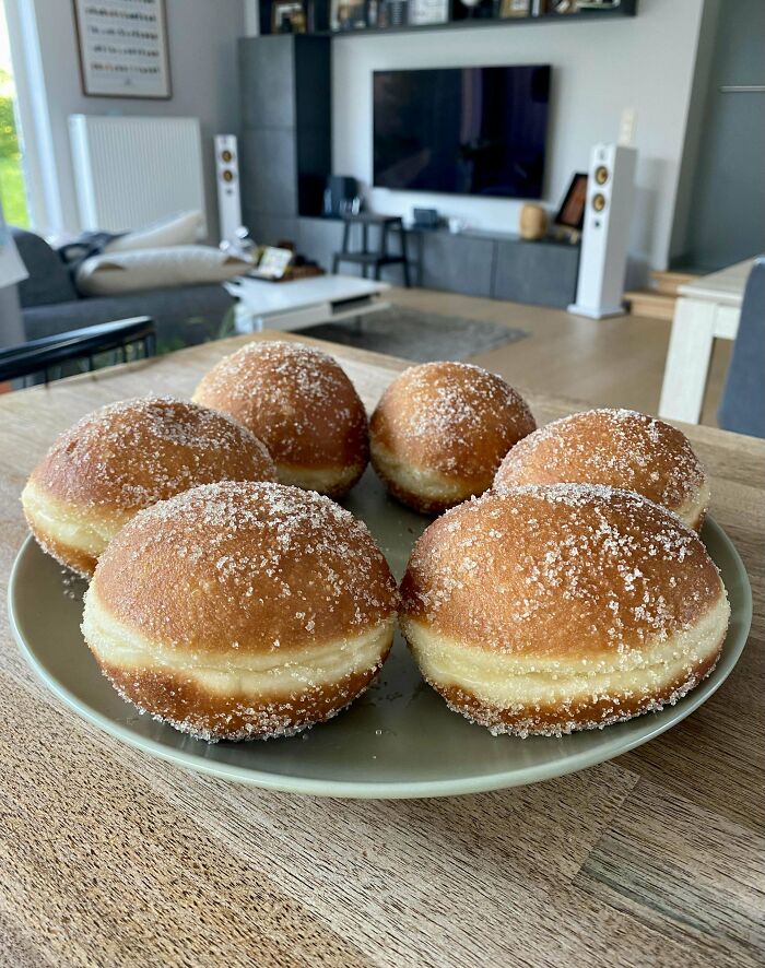 Six sugar-coated baked donuts on a plate in a modern living room setting, showcasing baking at its finest.