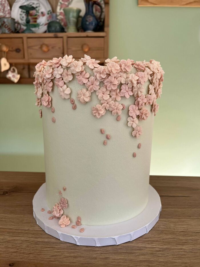 Tall white cake decorated with delicate pink flowers, showcasing elegant baking at its finest on a wooden table.