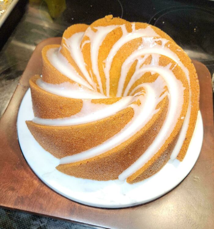 Swirled bundt cake with white glaze on a plate, showcasing baking at its finest with a moist golden-brown texture.