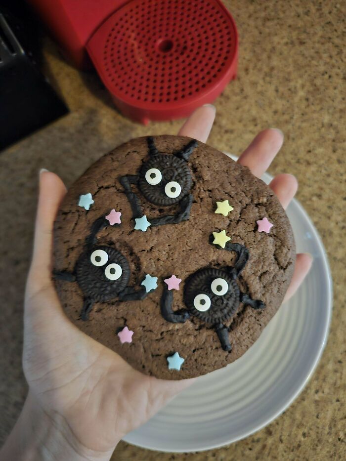 Large decorated chocolate cookie with Oreos and colorful star sprinkles held over a plate, showcasing baking at its finest.