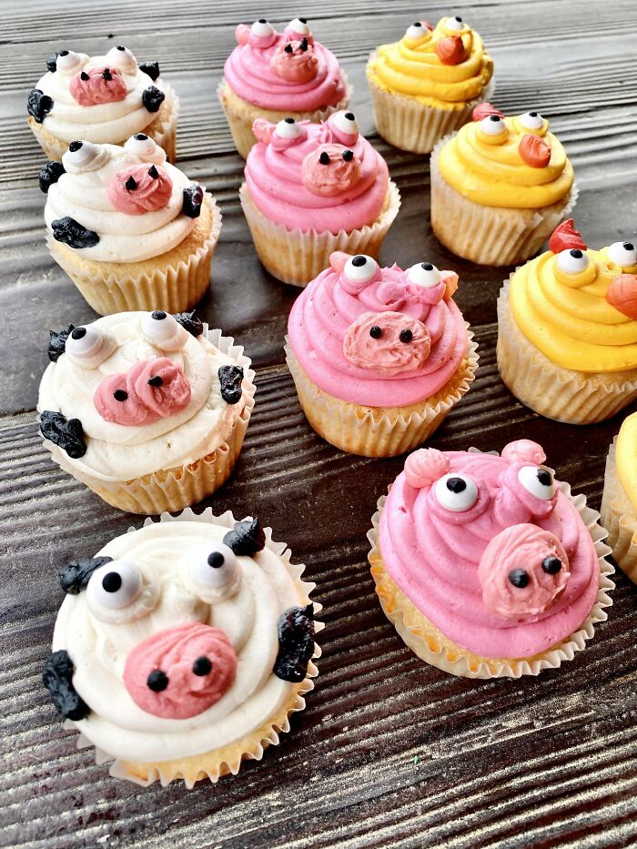 Cupcakes decorated as pigs, cows, and chicks with colorful frosting on a wooden surface, showcasing creative baking designs.