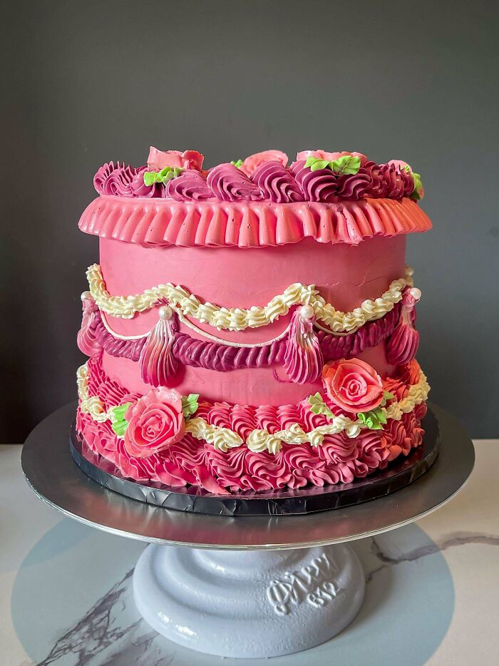 Pink decorated cake with piped frosting rosettes and swirls on a white cake stand, showcasing baking at its finest.