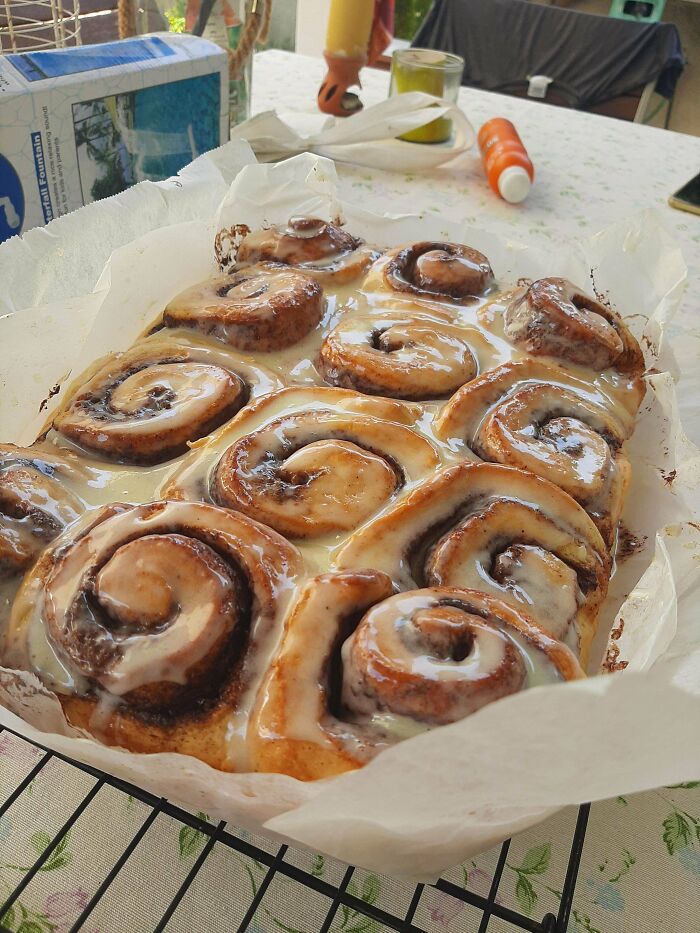 Freshly baked cinnamon rolls glazed with creamy icing, showing baking at its finest on a parchment-lined tray.