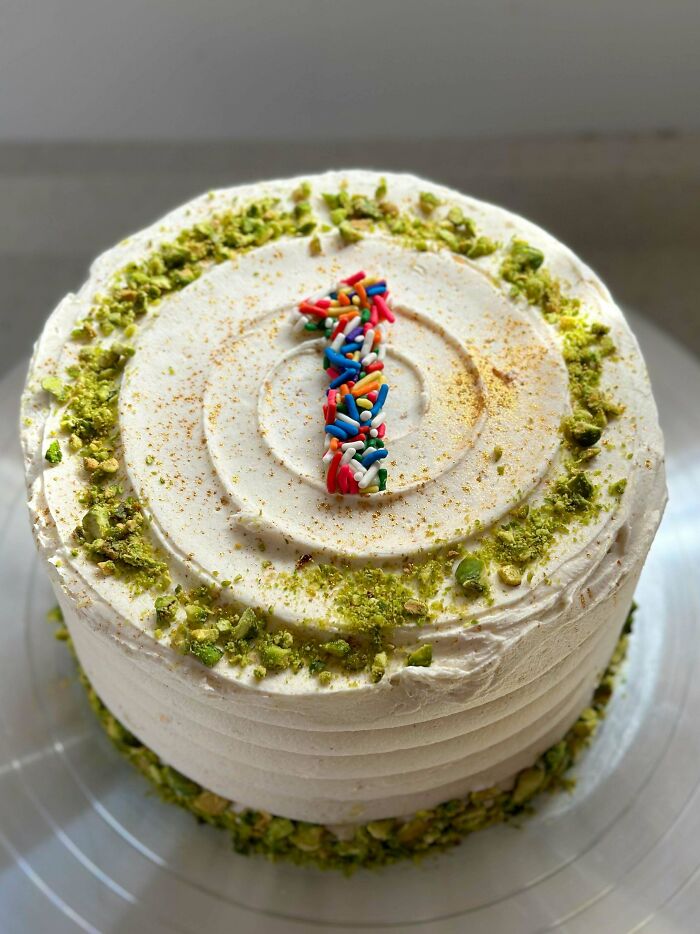 Round cake with creamy frosting decorated with crushed pistachios and colorful sprinkles in the shape of the number one, baking at its finest.