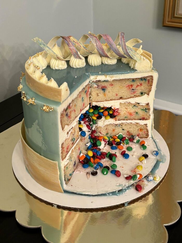 A colorful pinata cake with layers of confetti baking at its finest, decorated with blue icing and cream swirls.