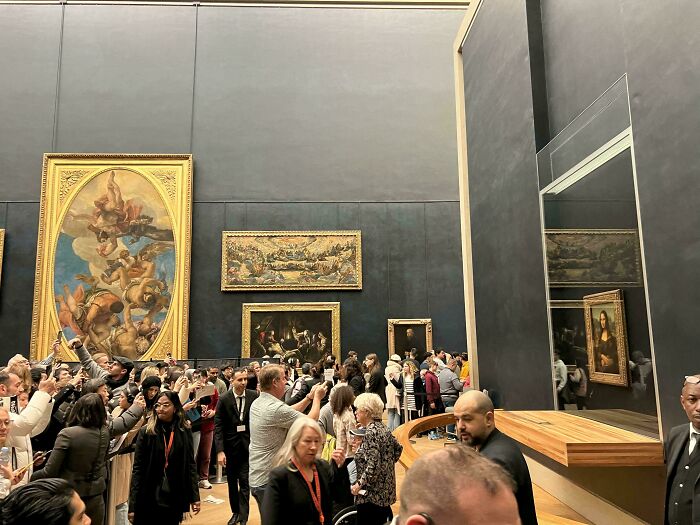 Crowd viewing famous art in a museum with glass protection, offering a new perspective on famous places.