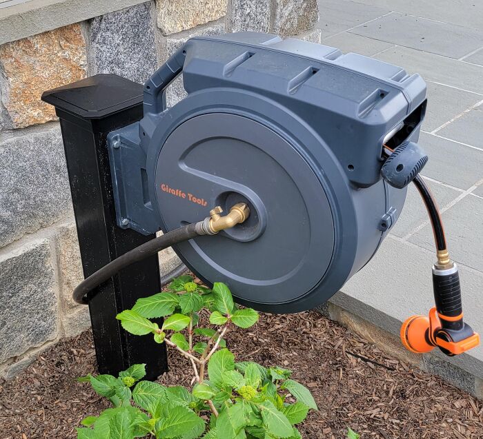 Outdoor hose neatly stored on a retractable reel mounted on a post, demonstrating a genius hack for hiding ugly garden tools.