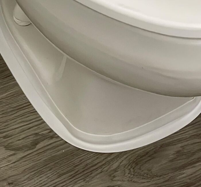 Close-up of a white plastic tray placed under a toilet to hide ugly bathroom floor stains and imperfections.