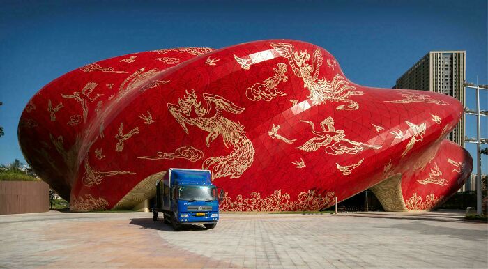 Bizarre building with a bold red exterior decorated with golden dragon designs next to a blue truck under clear skies.
