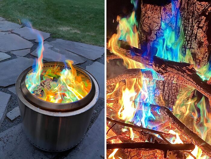 Colorful blue and green flames burning in a stainless steel fire pit near garden stone pavers and grass lawn outdoors.