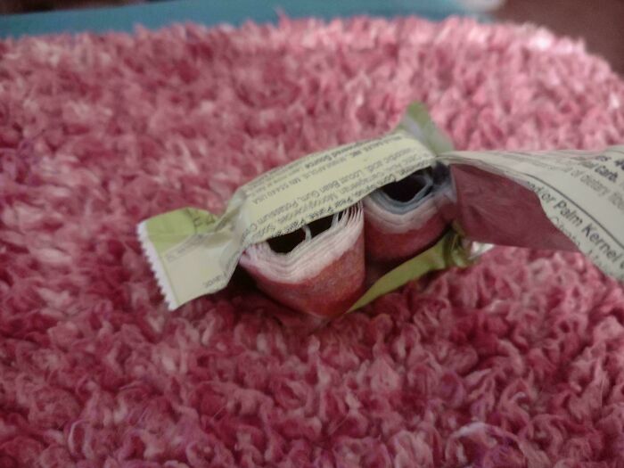Extra candy rolls spilling out of an opened wrapper on a fluffy pink surface.