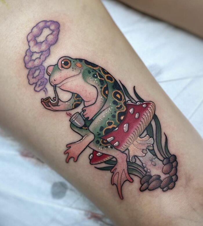 Creative frog tattoo with a pipe and mushroom on forearm.