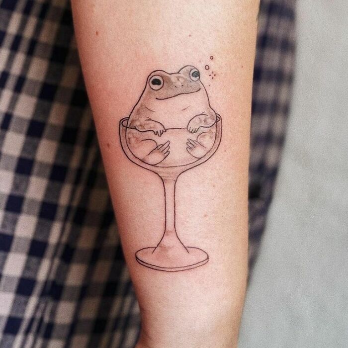 Frog tattoo in a glass inked on an arm, showcasing creative and adorable design.