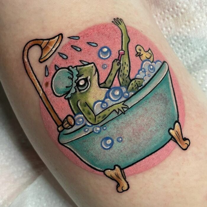 Creative frog tattoo with frog in a bathtub, wearing a shower cap, surrounded by bubbles and a rubber duck.
