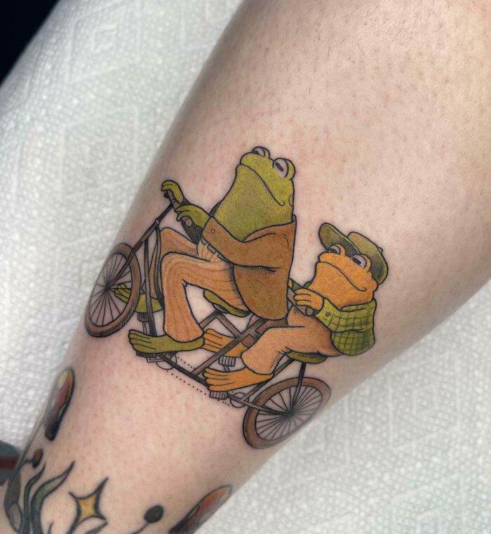 Creative frog tattoo of two frogs riding a tandem bicycle, showcasing awesome and adorable design elements on skin.