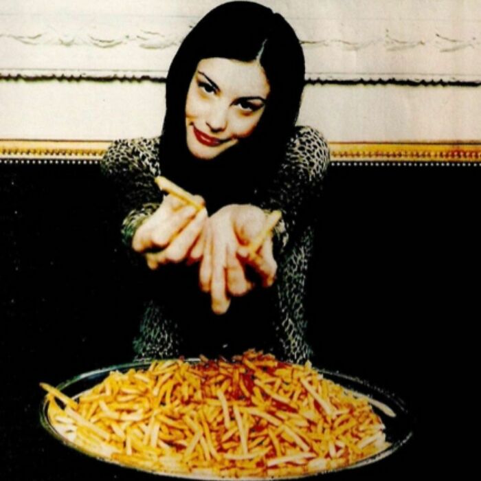Woman in a leopard print top playfully offering fries from a large plate; '90s vibe captured.