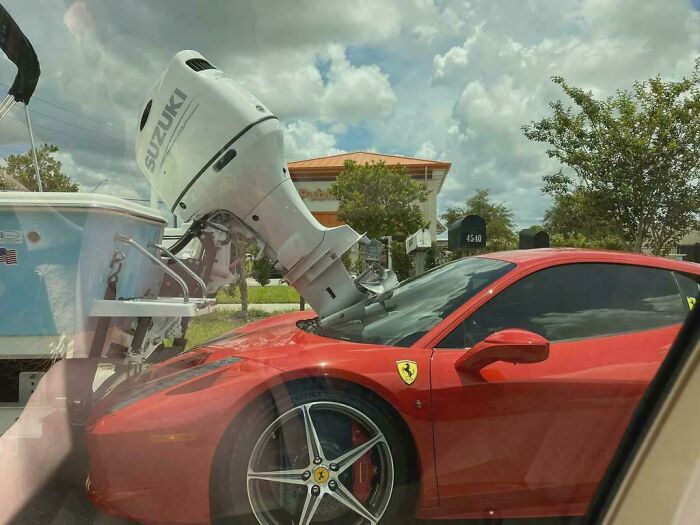 A red sports car is hit by a large boat motor, showcasing an unfortunate and expensive incident.