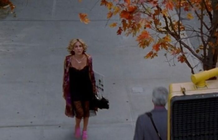 Woman in '90s fashion walks on a sidewalk with autumn leaves above, capturing a wild and wholesome era moment.