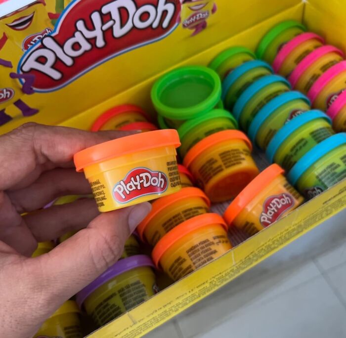 Hand holding a small Play-Doh container among colorful non-candy treats in a box for Halloween gift ideas.