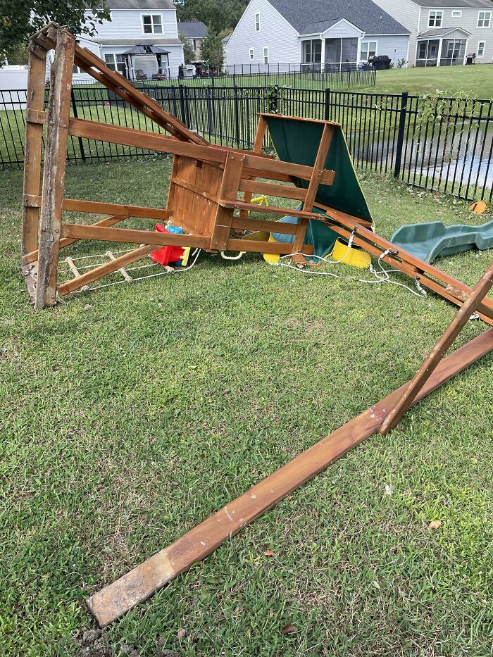 Wooden backyard playset collapsed on grass showing funny dads doing their best home repair efforts.