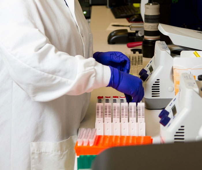 Scientist wearing gloves handling test tubes in a lab, uncovering chilling truths hidden in plain sight after death.