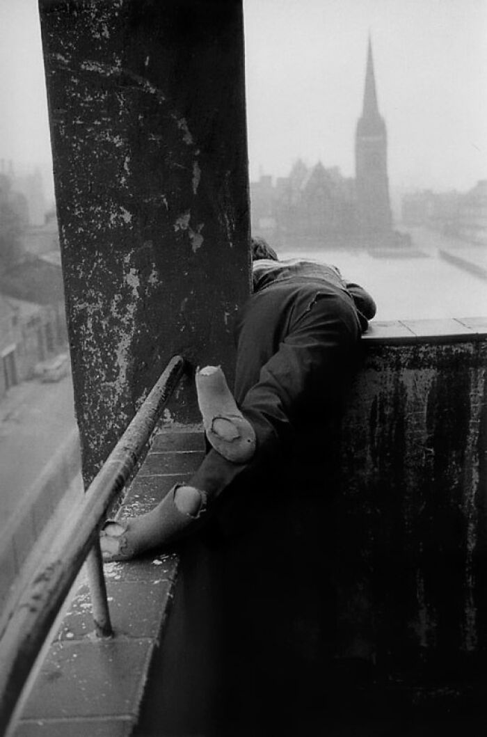 Child with worn socks leaning over a ledge in a vintage black and white historical photo from a FB group collection.