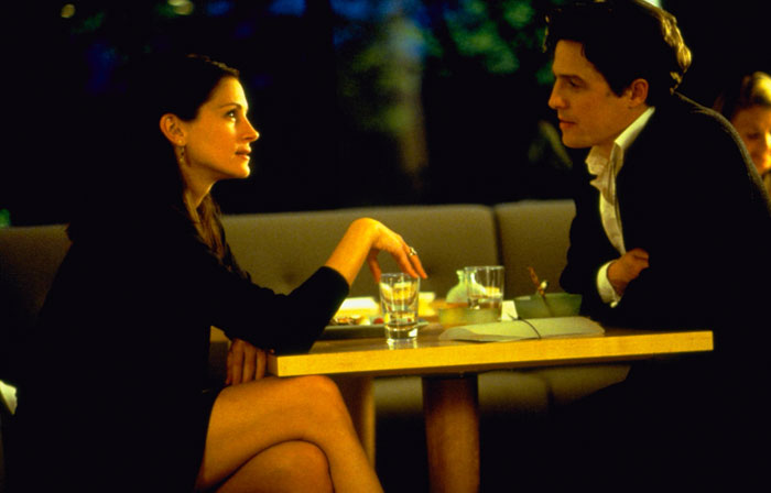 A scene from the movie Notting Hill featuring a man and a woman sitting across from each other at a small table in a dimly lit restaurant. The woman, dressed in a black outfit, leans forward slightly, engaging in conversation, while the man, wearing a suit, listens attentively with a thoughtful expression. Glasses of water and a notebook are placed on the table between them, creating an intimate and quiet atmosphere. A scene from the movie Notting Hill featuring a man and a woman sitting across from each other at a small table in a dimly lit restaurant. The woman, dressed in a black outfit, leans forward slightly, engaging in conversation, while the man, wearing a suit, listens attentively with a thoughtful expression. Glasses of water and a notebook are placed on the table between them, creating an intimate and quiet atmosphere.