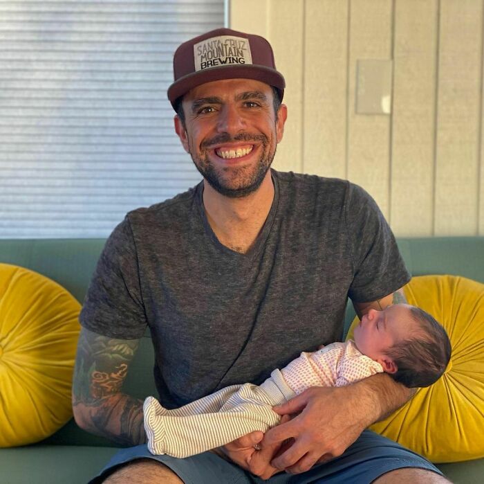 Man with a hat smiling and holding a sleeping baby, capturing one of the most moving stories from Humans of New York.