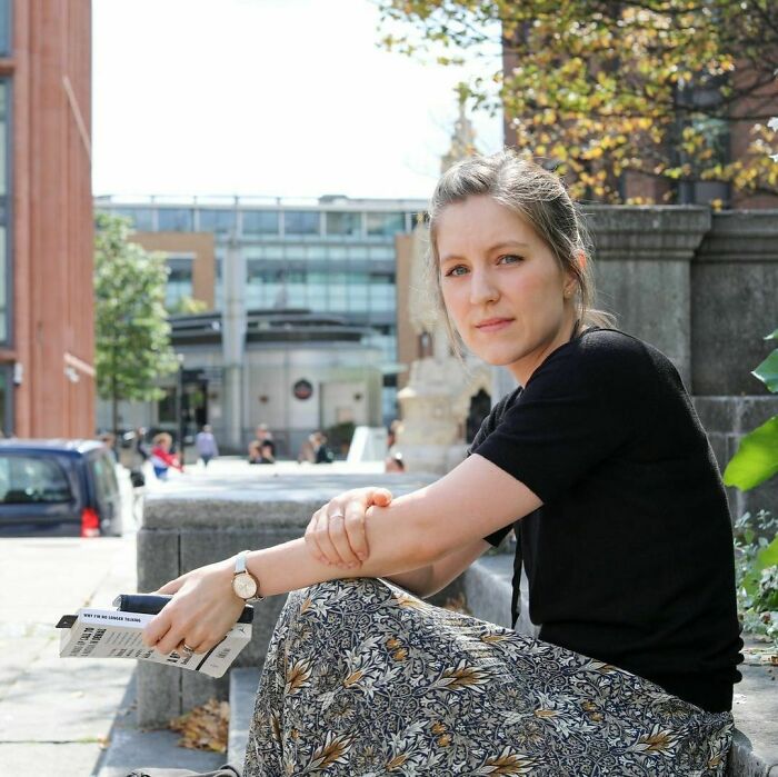 Young woman sitting outdoors reading, captured in a candid moment, reflecting the moving stories of Humans of New York.